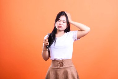 Siyah boş bir cüzdan tutan ve yüzünde üzgün bir ifadeyle kafasına dokunan bir kadın, turuncu arka planda soyutlanmış..