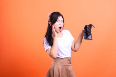 Turuncu arka planda sürpriz bir ifadeyle boş bir siyah cüzdan tutan bir kişi..