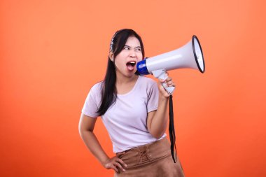 Bir kadın elinde beyaz bir megafon tutuyor, ağzı açık bağırıyor, turuncu bir arka planda izole bir şekilde..