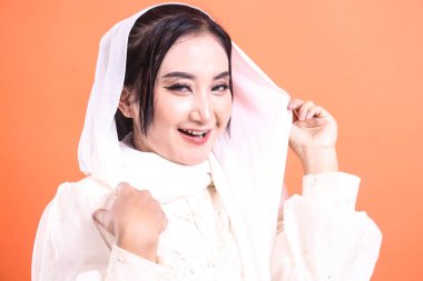 Beyaz tesettürlü güzel bir Müslüman kadının portresi kameraya gülümsüyor ve özgüvenle poz veriyor. turuncu bir arkaplanda izole.