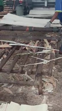 Bir işçi, kontrplak fabrikasındaki ahşap kaplamaları üretmek için makineler kullanıyor. Bu da sanayi sürecini ve marangozluk sektöründeki kaynak yönetimini gösteriyor..