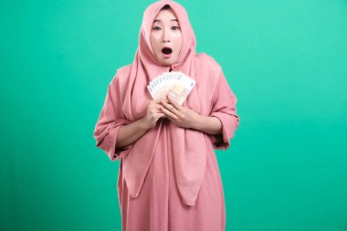 Şok olmuş Müslüman bir kadın ağzı açık ve hayret verici bir ifadeyle elinde avroya ait banknotlarla yeşil bir arka planda izole edilmiş başarıyı ve finansal bolluğu kutluyor..