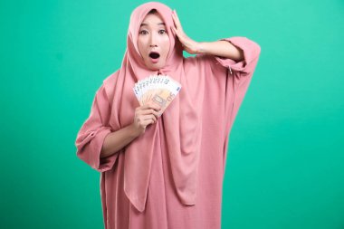 Avro banknotlarını kavramış, yeşil arka planda izole edilmiş, mali zaferinden duyduğu büyük neşeyi dile getiren, şok olmuş Müslüman bir kadın. Finansal kazançları onu şaşırttı ve heyecanlandırdı..