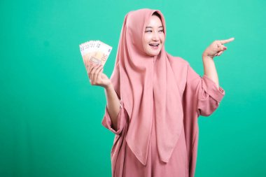 Tesettürlü mutlu Müslüman kadın avro banknotları tutuyor ve yeşil bir arkaplanda izole edilmiş, gelecekteki yatırımlara ve fırsatlara işaret ediyor..