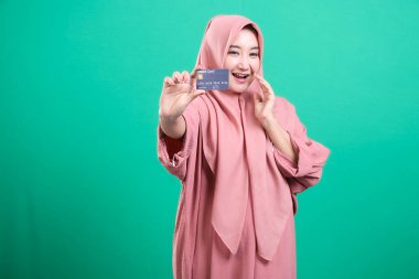 Stüdyo ortamında banka kartını sunan neşeli ve modern Müslüman bir kadının portresi yeşil bir arka planda izole edilmiş. Çevrimiçi alımından memnun ve tekrar alışveriş yapmaya hazır..
