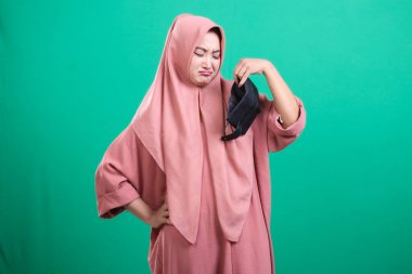 Salgın bittikten sonra kullanmamaktan iğrenen, yeşil arka planda izole edilmiş, sağlıksız ve rahatsız hisseden, yüz maskesi tutan mutsuz müslüman kadın..