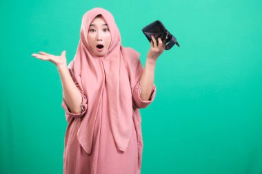 Kafası karışmış tesettürlü bir kadının yeşil arka planda izole edilmiş perişan bir ifadeyle boş bir cüzdan taşıdığı görülüyor. Ekonomik kriz konusunda endişeli görünüyor..