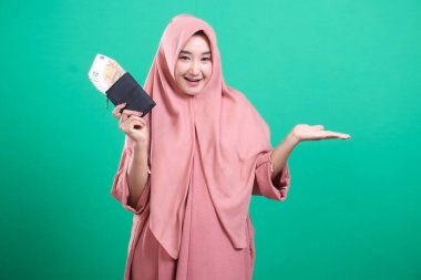 Para dolu cüzdanı olan genç Müslüman bir kadın yeşil bir geçmişe izole edilmiş bir jest yapıyor. Başarıyı ve finansal özgürlüğü simgeliyor.