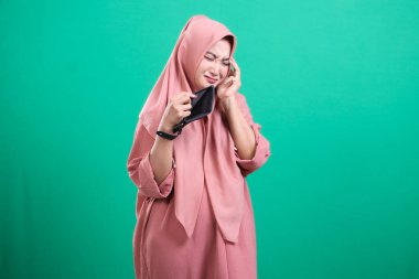 Boş cüzdanını kontrol eden tedirgin bir kadın, ekonomik sıkıntıları ve yeşil arka planda izole edilmiş fon eksikliğini gösteriyor..