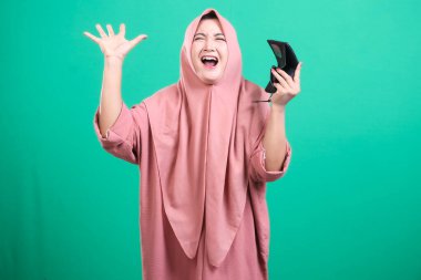 Başörtüsü olan üzgün bir Müslüman kadın, yeşil bir arka planda izole edilmiş, parasızlıktan hayal kırıklığına uğramış ve şok olmuş bir şekilde cüzdanını kaldırıyor..