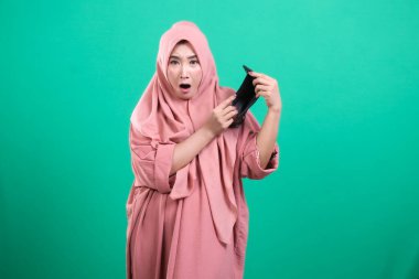 Perişan bir Müslüman kadın, yeşil arka planda izole edilmiş kişisel ekonomik krizi simgeleyen boş bir cüzdan tutarak mali sıkıntısını ifade ediyor..