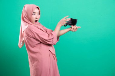 Boş cüzdanını gösteren bir kadın, mali durumundan duyduğu üzüntüyü dile getiriyor. Ekonomik kaygılara işaret ediyor, yeşil bir arka planda izole edilmiş..