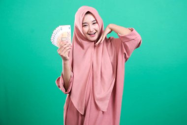 Avro banknotları tutan neşeli genç Müslüman kadın, yeşil bir geçmişe izole edilmiş, modern bağlamda refah ve ekonomik başarıyı gösteren mali başarısını dile getiriyor.