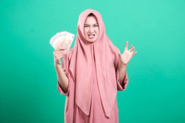 Başörtüsü takan bir kadın, avro banknotlarını elinde tutarken, yeşil arka planda izole edilmiş mali sorunlara karşı korku ve kızgınlığını dile getiriyor.