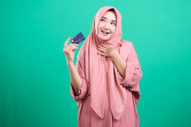 Yeşil arka planda izole edilmiş mutlu ve heyecanlı bir yüz ifadesi olan tesettürlü, tesettürlü güzel, modern Müslüman kadın. Son online alımından çok etkilenmiş görünüyor..