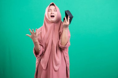 Çaresiz Müslüman kadın boş bir cüzdan gösteriyor. Ekonomik sıkıntıları ve ekonomik sıkıntıları vurguluyor. Yeşil bir arka planda izole edilmiş..