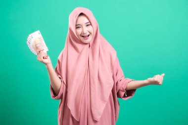 Başörtüsü takan mutlu bir Müslüman kadın bir yığın avro banknotu tutuyor ve gülümsüyor, kendini zengin ve yeşil bir arka planda soyutlanmış hissediyor. Portre başarılı, şanslı ve varlıklı bir bayanı gösteriyor.