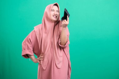 Hüsrana uğramış ve tesettürlü bir kadın, yeşil arka planda izole edilmiş mali zorluk ve hayal kırıklığını tasvir ederek cüzdanını boş bulmaktan duyduğu hayal kırıklığını dile getiriyor. Maddi sorunları ve potansiyel iflası temsil ediyor. Sıkıntılı bir yüz tanıma programıyla