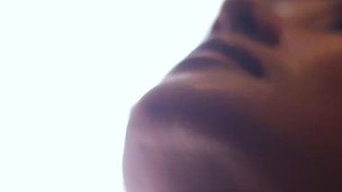 Cilt bakımını ve yüz hatlarını vurgulayan, parlak bir arkaplana bakan bir kadının yakın çekim görüntüsü,