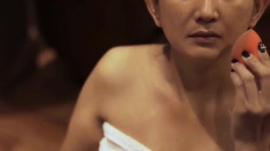 Zarif Asyalı kadın makyajını süngerle yapıyor, doğal güzelliğini geliştiriyor ve bir an için kendine bakmasını sağlıyor.