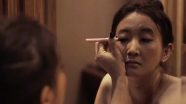 Aynanın önüne göz kalemi süren bir kadın makyaj dersleri için güzellik rutinini yakalıyor.