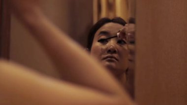 Aynanın karşısına maskara süren bir kadının estetik görüntüsü kişisel bakım ve güzelliği yansıtıyor.