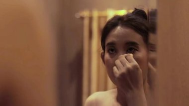 Sıcak bir odada makyaj yapan, aynaya yansıyan, güzellik gösteren bir kadının yakın plan çekimi.