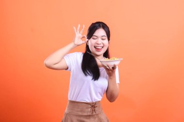 Gülümseyen ve elinde bir kase erişte tutan genç bir kadın lezzetli bir yemekten sonra tatmin olmuş görünüyor. turuncu arkaplanda izole