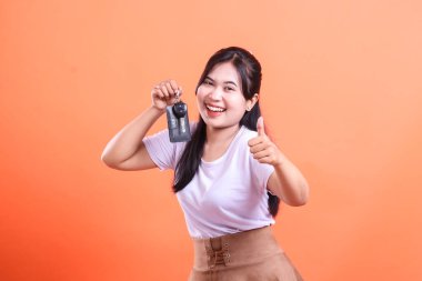 Mutlu genç bir kadın arabanın anahtarını gösteriyor ve yeni arabayı aldıktan sonra heyecanını dile getiriyor. turuncu arkaplanda izole.