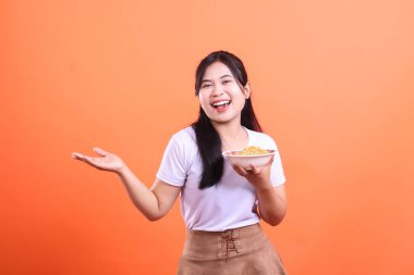 Genç ve güzel bir kadın bir kase erişteyi gülümseyerek sunuyor, mutlu görünüyor. turuncu arkaplanda izole