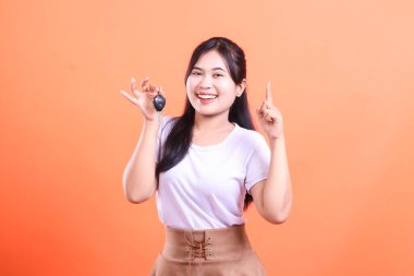 Heyecanlı genç bayan gururla araba anahtarlarını sunuyor, yeni anahtarı elinde tutuyor, gülümsüyor. turuncu arkaplanda izole.