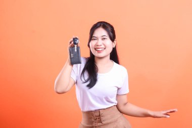 Neşeli genç Asyalı bir kadın araba anahtarını tutarken gülümsüyor. Turuncu arka planda izole edilmiş.