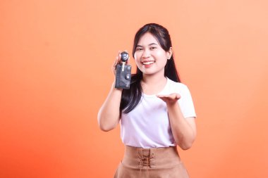 Araba anahtarı tutan ve diğer eliyle el kol hareketi yapan gülümseyen genç bir kadın. Turuncu arka planda izole edilmiş..