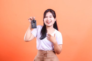 Çekici genç Asyalı kadın yeni araba anahtarlarını tutarken mutlu bir şekilde gülümsüyor, çok mutlu görünüyor. turuncu arkaplanda izole