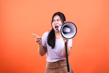 Bir kadın turuncu arka planda megafona bağırıyor, tek eliyle bir tarafı işaret ediyor..