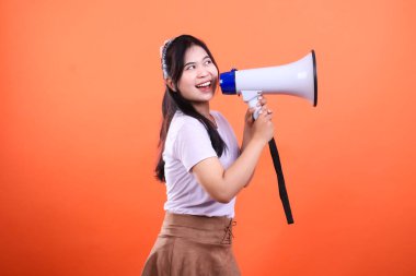 Bir kadın elinde beyaz bir megafon tutuyor, ona doğru konuşuyor ve yukarı bakıyor. Görüntü turuncu bir arkaplanda izole edilmiş..