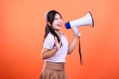 Bir kadın elinde megafon tutuyor. O, beyaz bir tişört ve kahverengi bir etek giyiyor. Turuncu bir arka planda izole edilmiş..