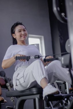 Spor kıyafetleri içinde gülümseyen bir kadın bir spor salonu ortamında spor salonunda spor yapmaya ve sağlığına bağlılık yemini ediyor..