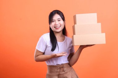 Sevkiyata hazır, turuncu arka planda izole bir şekilde el kol gezen neşeli bir kadın.