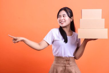 Elinde bir yığın kutu tutan neşeli bir kadın ve bir tarafı işaret eden, reklam dağıtım servisi. turuncu arkaplanda izole