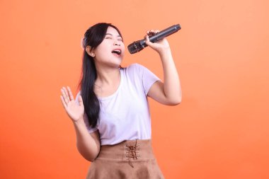 İçi enerji ve tutkuyla dolu, mikrofonla şarkı söyleyen hevesli genç bir kadın. turuncu arkaplanda izole