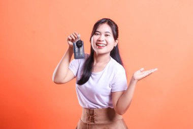 Neşeli kadın arabanın anahtarını tutuyor ve gülümseyerek el kol hareketi yapıyor. turuncu arkaplanda izole.