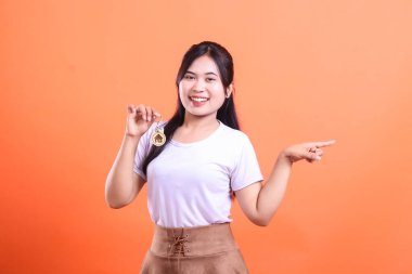 Neşeli genç bir kadın, başarısının bir sembolü olan geleceği gösteren yeni ev anahtarlarını gururla sergiliyor. turuncu arkaplanda izole