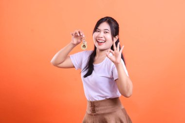 Gülümseyen kadın yeni evinin anahtarlarını gururla sergiliyor. Olumlu bir jest yaparak turuncu arka planda izole edilmiş yeni alımın heyecanını gösteriyor.