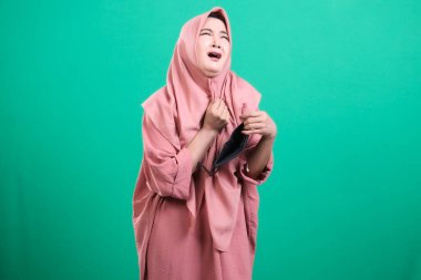 Sıkıntılı, tesettürlü, sıcakla boğuşan, yeşil arka planda izole bir Müslüman kadın. Sıcak havanın verdiği rahatsızlığı ve yeşil arka planda izole edilmiş solunabilir giysi ihtiyacını yaşamak..