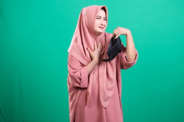 Başörtüsü takan bir kadın, boş cüzdanından yayılan kötü kokudan tiksinir, hayal kırıklıklarını aktarır, yeşil bir arka planda izole olur. Bu finansal zorlukları temsil ediyor..