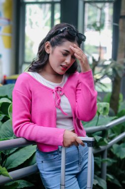 Çaresiz genç bir kadın trabzana eğilir, bavulu çekilir, eli alnına dokunur. İfadesi, botanik açısından zengin bir iç mekan ortamında büyük ihtimalle seyahat komplikasyonlarıyla ilgili derin bir hayal kırıklığı yaratıyor..