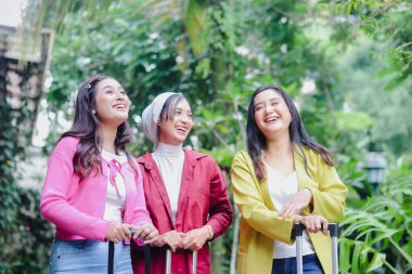 Sevinçle dolu üç şık genç kadın seyahat etmeye hazır. Bavullarını taşıyarak ve büyük bir gülümsemeyle yukarıya doğru bakıyorlar, hedeflerini keşfetmek için sabırsızlanıyorlar..