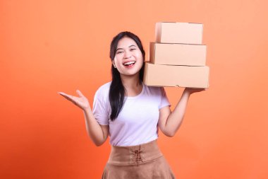 Neşeli genç bir kadın elinde bir yığın karton kutu tutuyor ve onlara bir gülümseme sunuyor. turuncu arkaplanda izole