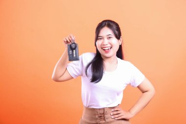 Neşeli genç bir kadın arabanın anahtarlarını gösteriyor ve geniş bir gülümseme sergiliyor, yeni bir araç, mülk satın alma ya da kira sözleşmesi sunuyor. turuncu arkaplanda izole.